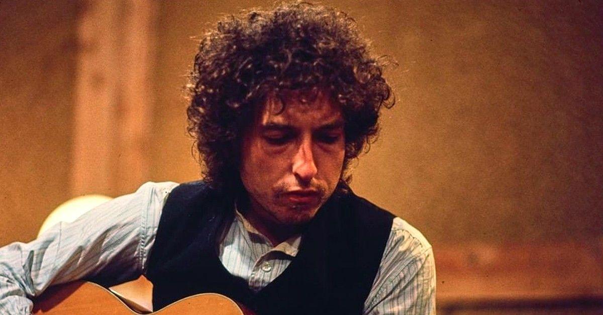 Bob Dylan em um colete preto tocando guitarra