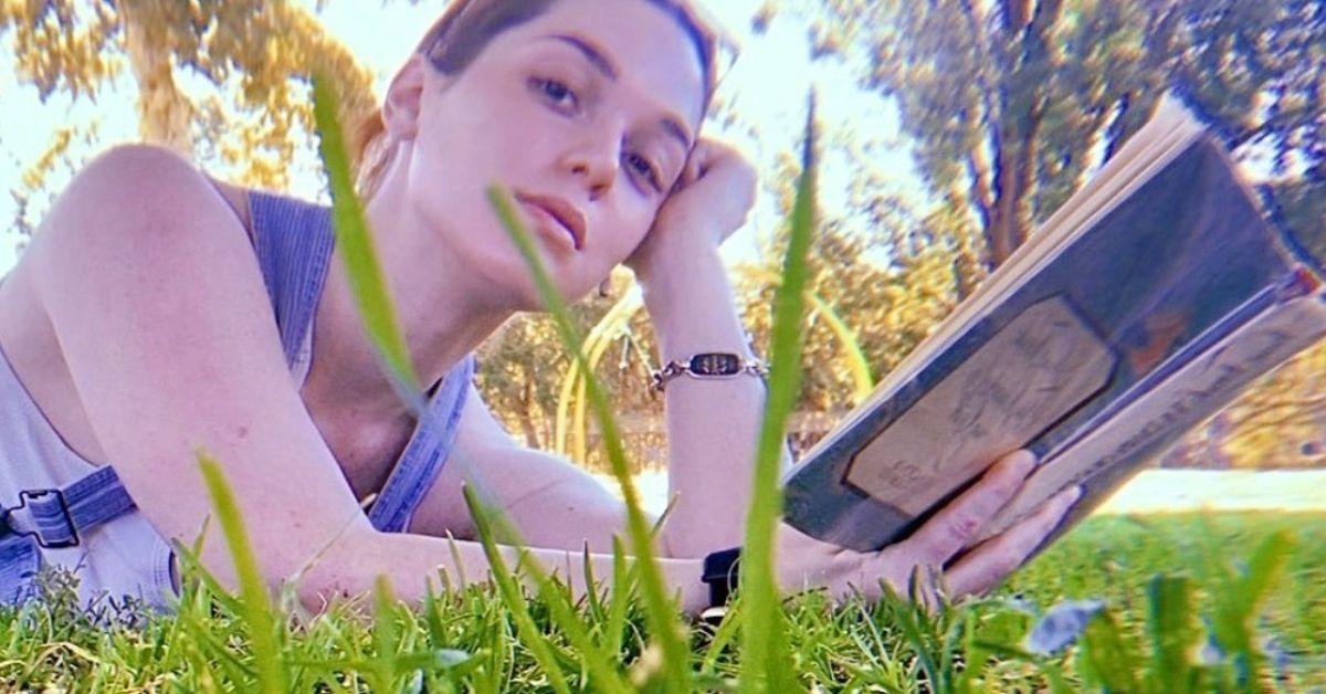 Jennifer Stone lendo em um parque e segurando um livro
