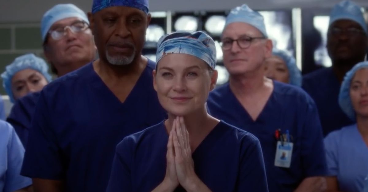 Ellen Pompeo como Meredith Gray em uma cena de Grey's Anatomy, orando com outros médicos ao seu redor.