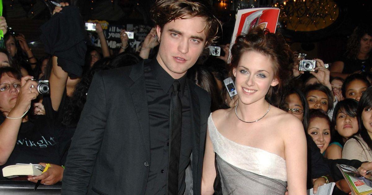 Robert Pattinson parecendo sério e Kristen Stewart sorrindo de pé juntos